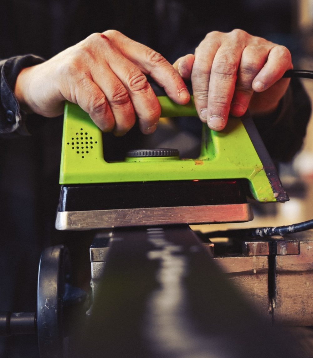 Two hands guiding the waxing iron over a ski held in a vice