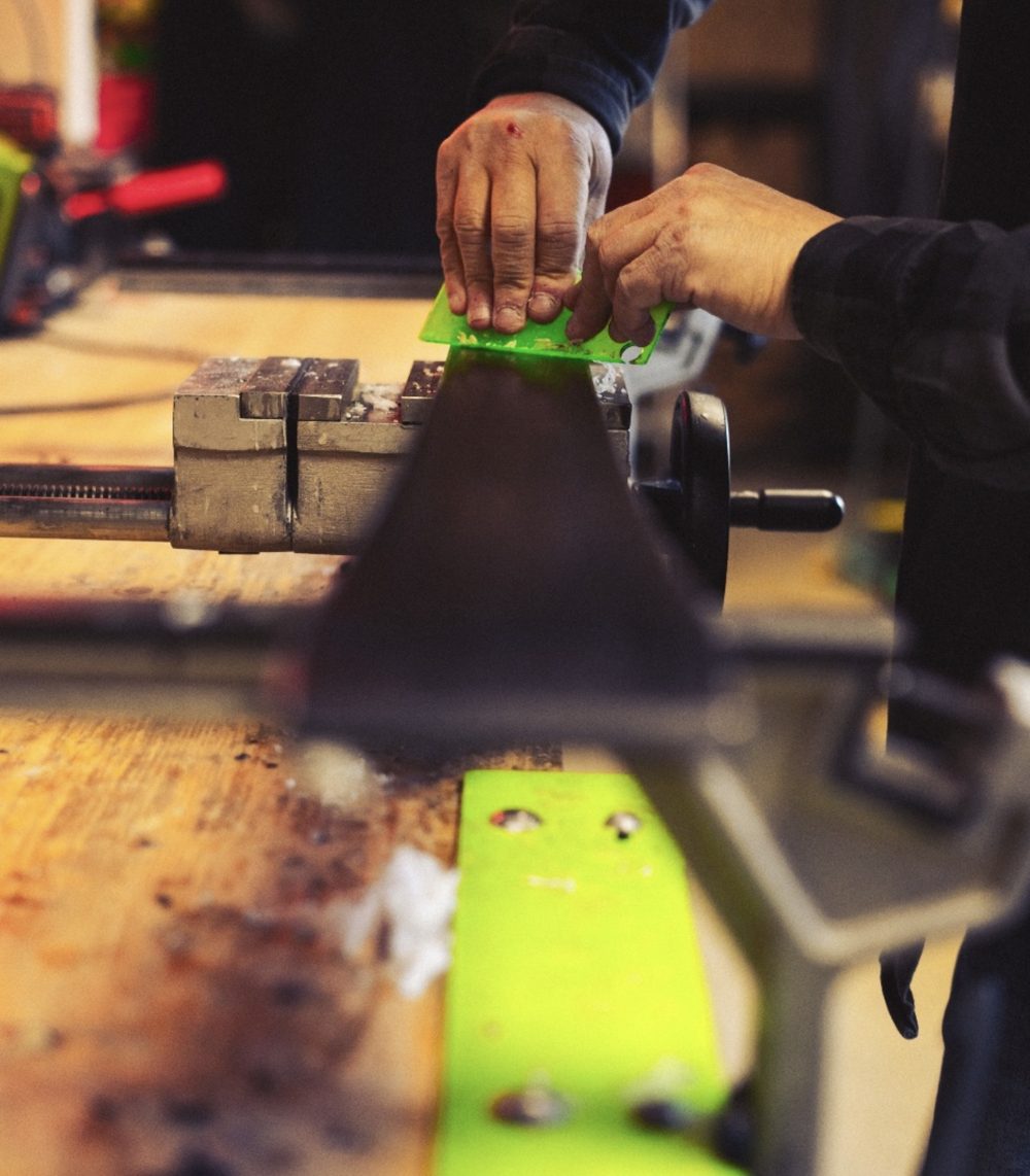 Green scraper removing excess wax from a ski in a vice