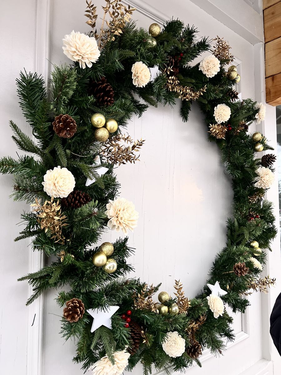 Couronne de sapin ornée de fleurs ivoire, de pommes de pin et de boules dorées sur la porte blanche