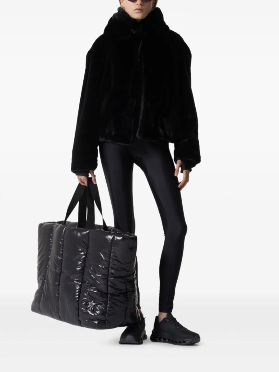 Veste noire à poils doux et capuche, portée avec un cabas matelassé